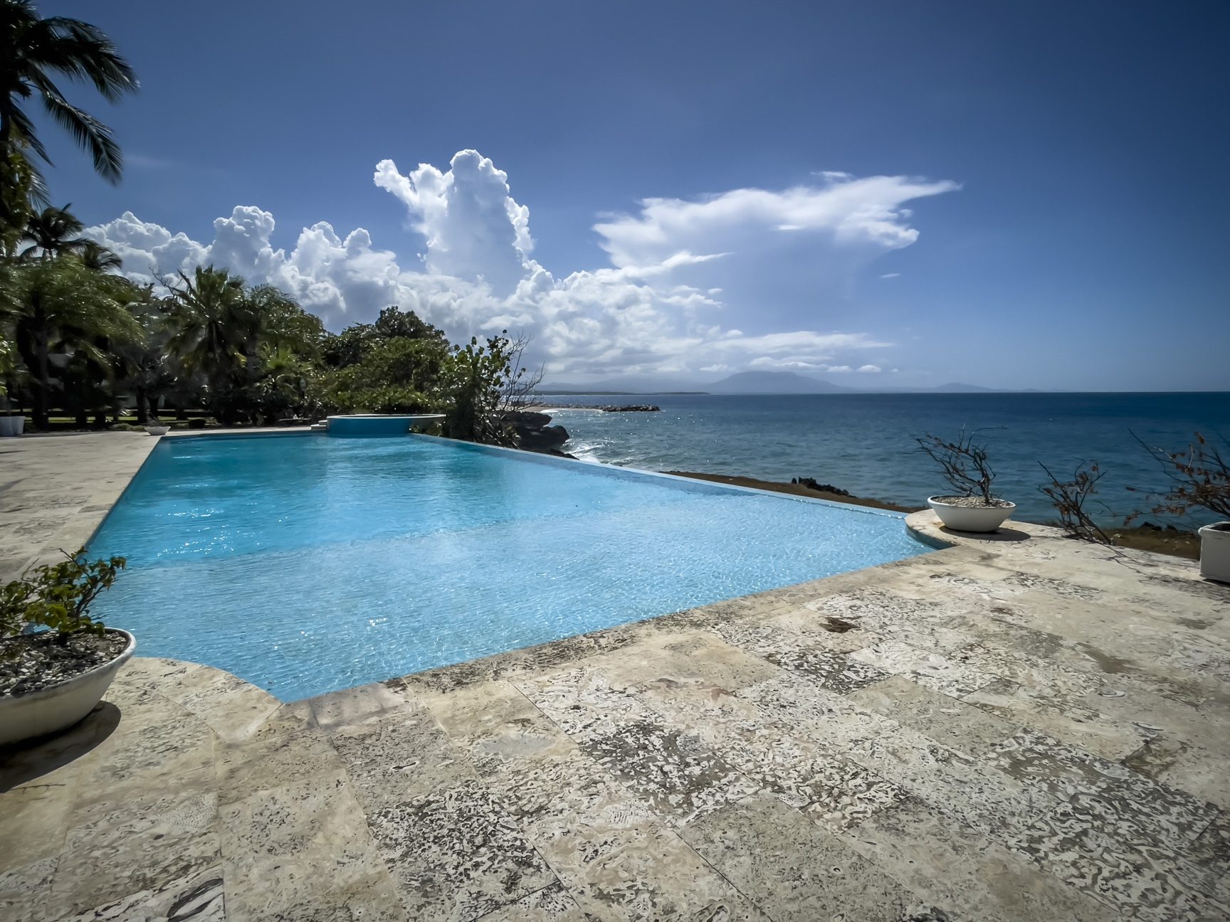 buyDRproperty Infinity pool overlooking the turquoise ocean under a partly cloudy blue sky Sosua Real Estate