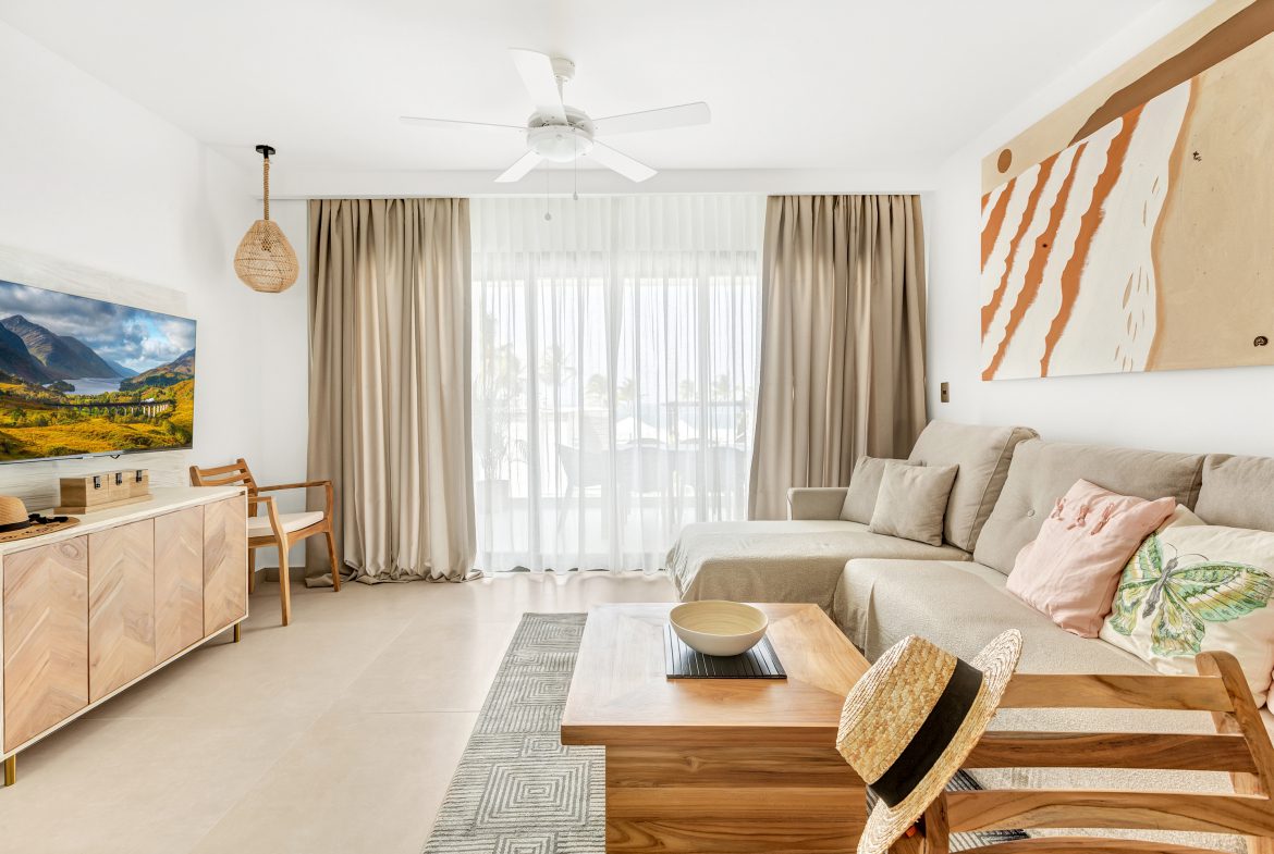 buyDRproperty Bright living room with sectional sofa, TV, and straw hats. Light and airy interior design. Sosua Real Estate