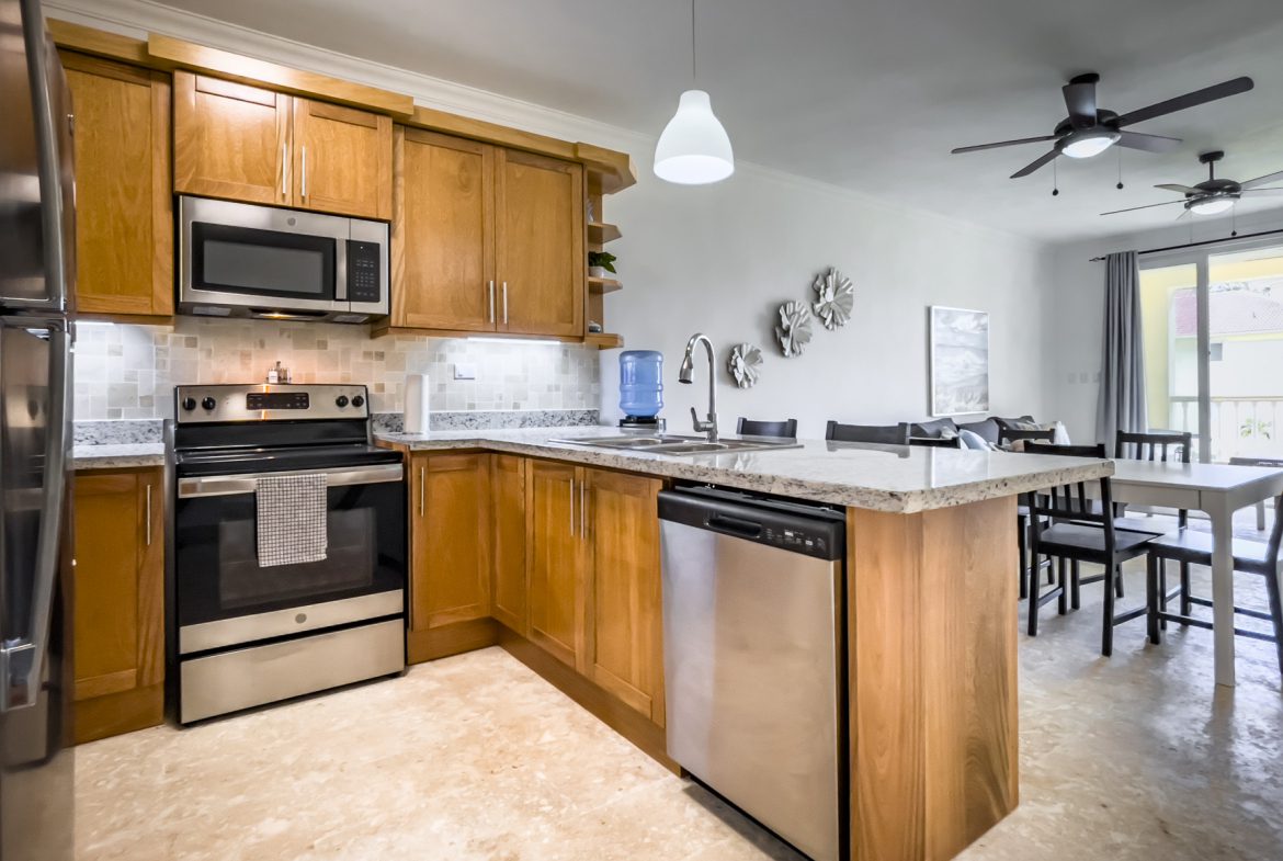 buyDRproperty Bright kitchen with wood cabinets, stainless steel appliances, and an island. Dining area visible. Sosua Real Estate