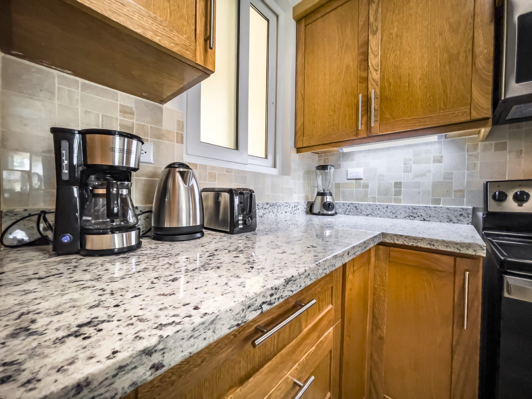 buyDRproperty Kitchen with granite countertops, wood cabinets, coffee maker, toaster, and stainless steel appliances. Sosua Real Estate