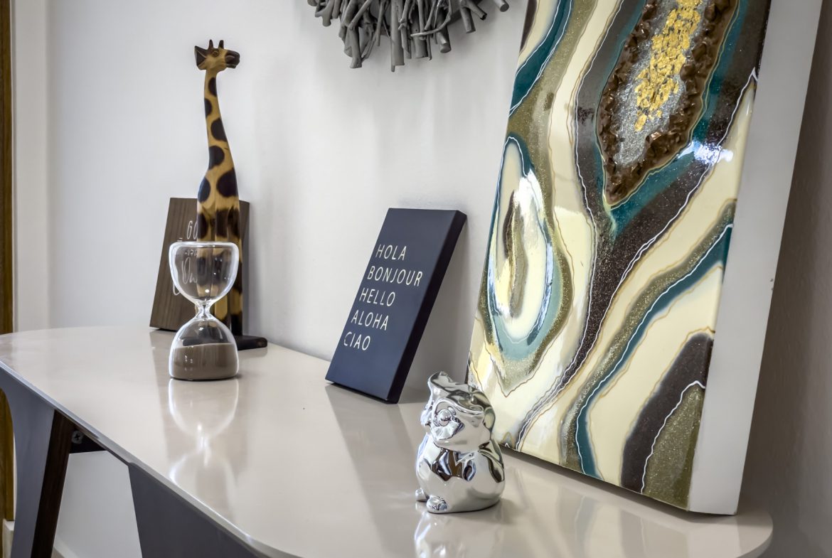buyDRproperty Stylish console table with decor: giraffe, hourglass, art, and a "Hola Bonjour Hello Aloha Ciao" sign. Sosua Real Estate
