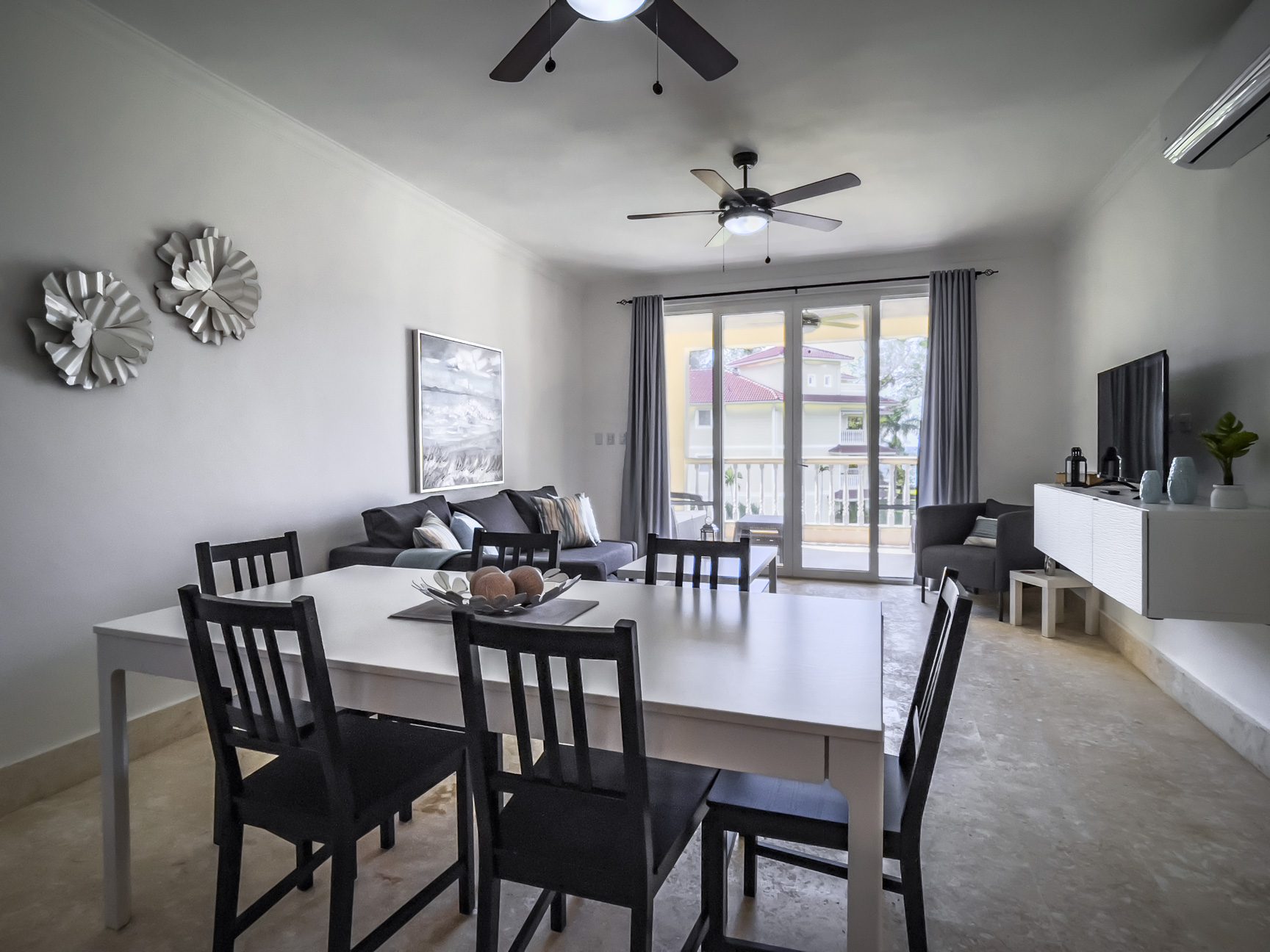 buyDRproperty Bright living room with white dining table, black chairs, and patio doors leading to a sunny outdoor area. Sosua Real Estate