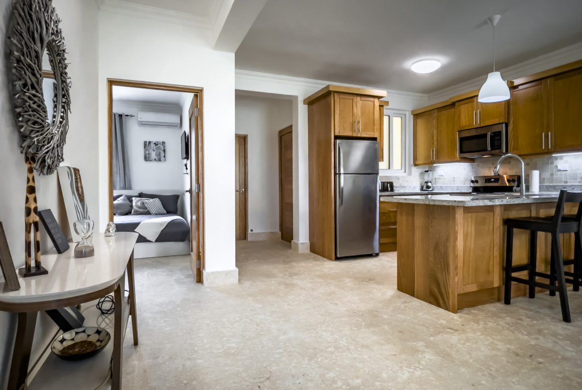buyDRproperty Modern apartment interior with kitchen, bedroom, and decor. Neutral tones and wood finishes create a warm atmosphere. Sosua Real Estate