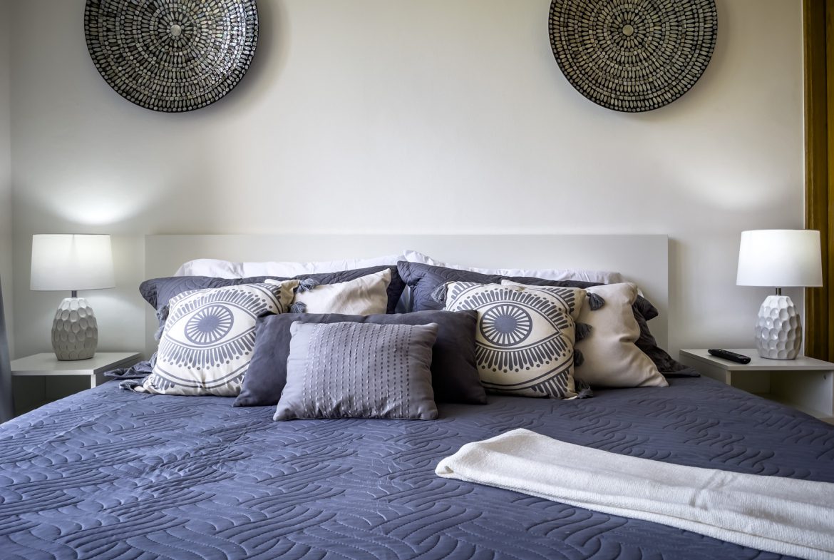 buyDRproperty Cozy bedroom with blue quilt, decorative pillows, and wall art. Sosua Real Estate