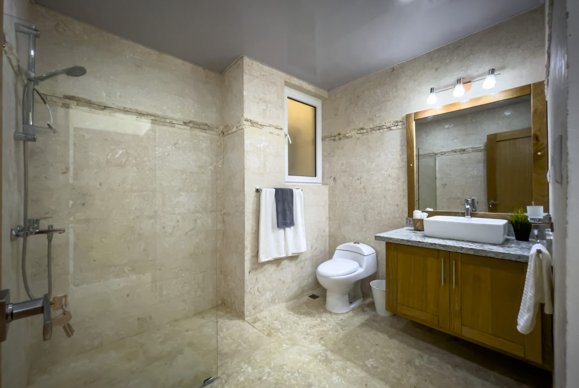 buyDRproperty Bathroom with walk-in shower, toilet, and vanity with wood cabinets and a stone countertop. Sosua Real Estate