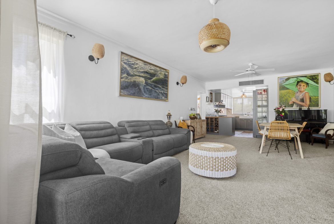 buyDRproperty Open-concept living room with gray sectional sofa, woven ottoman, and dining area with artwork. Sosua Real Estate