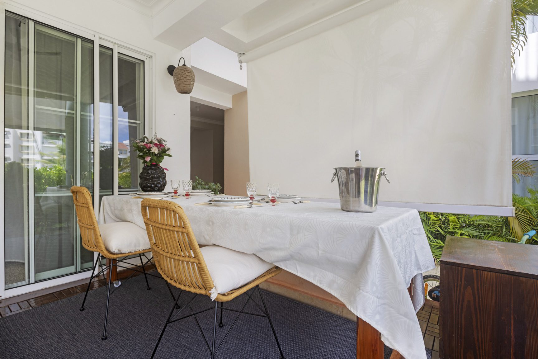 buyDRproperty Elegant outdoor dining setup with wicker chairs, white tablecloth, and wine cooler on a patio. Sosua Real Estate
