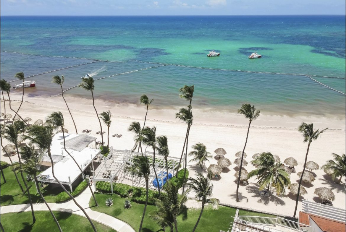 buyDRproperty Aerial view of a Caribbean beach resort with palm trees and turquoise water. Sosua Real Estate