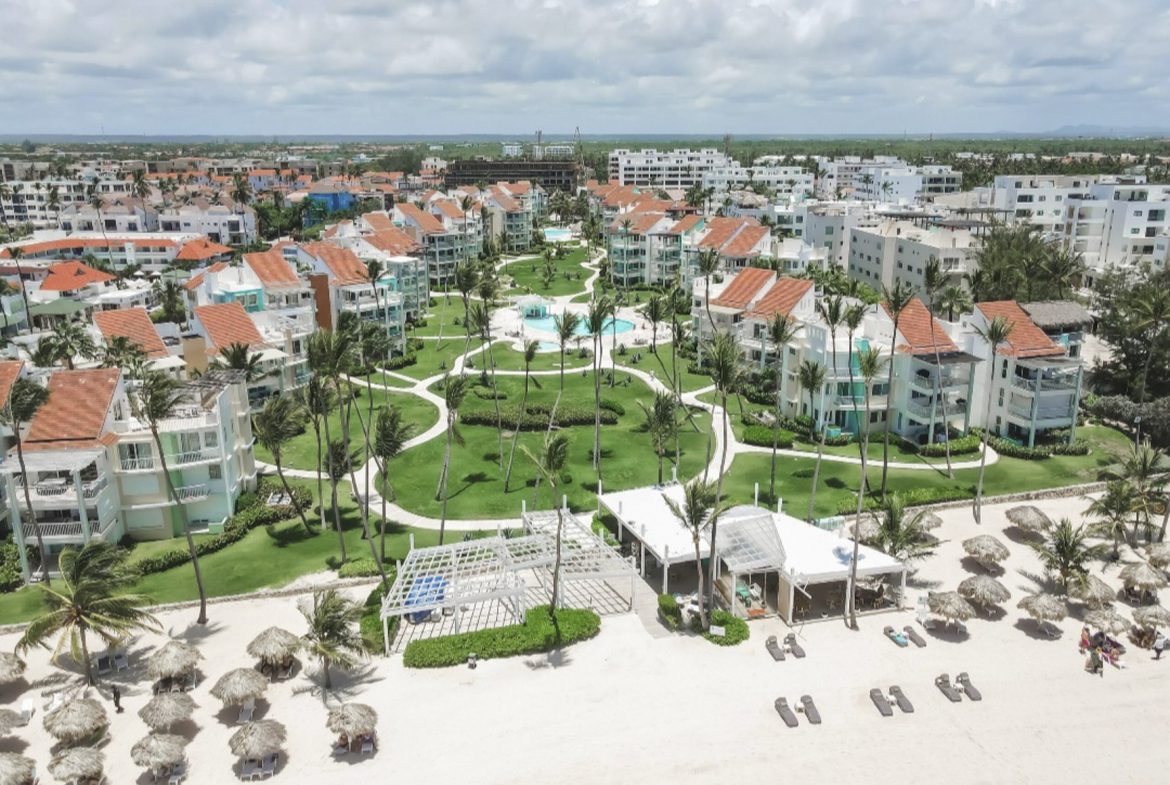 buyDRproperty Aerial view of a tropical resort with pools, palm trees, and beach umbrellas. Sosua Real Estate