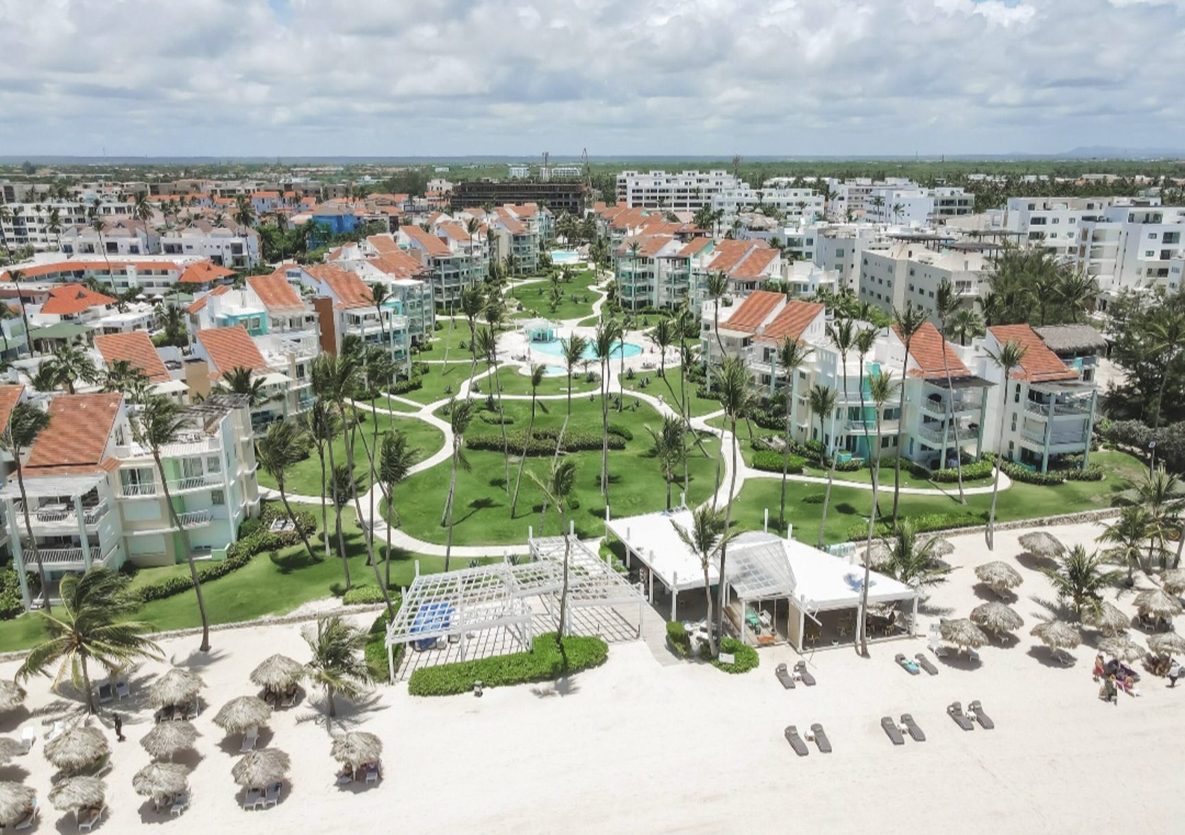 buyDRproperty Aerial view of a tropical resort with pools, palm trees, and beach umbrellas. Sosua Real Estate