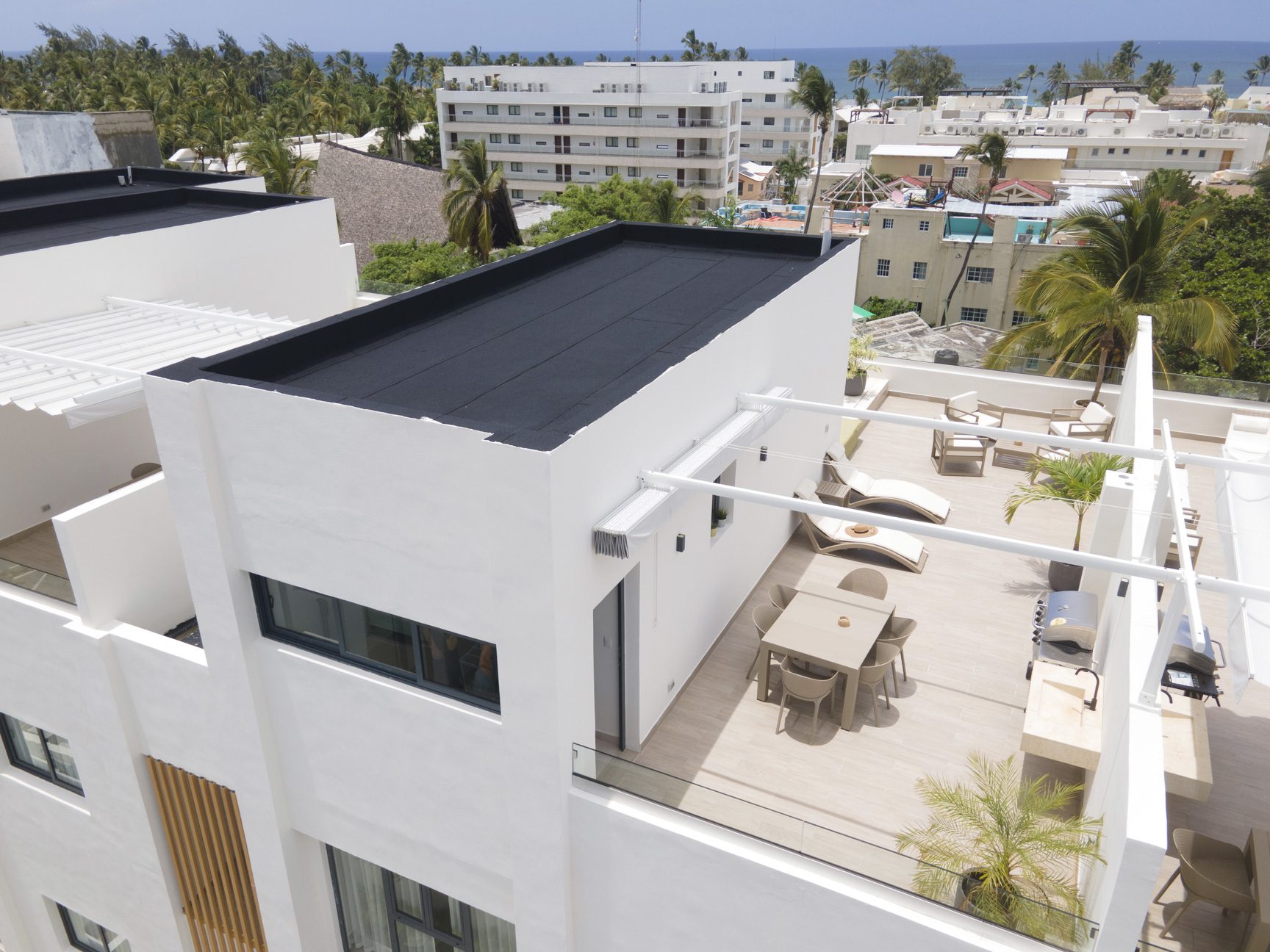 buyDRproperty Rooftop patio with modern furniture, palm trees, and ocean view in a tropical setting. Sosua Real Estate