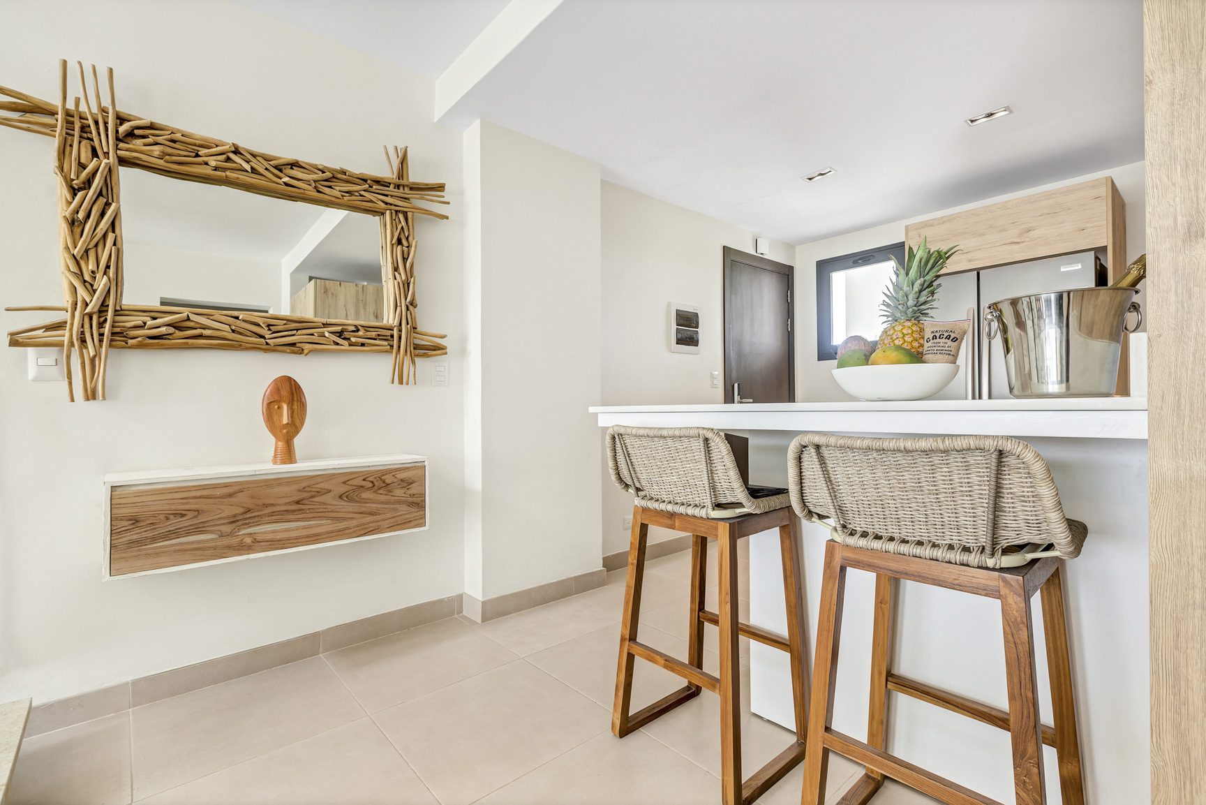 buyDRproperty Coastal kitchen with woven bar stools, driftwood mirror, fruit bowl, and modern decor. Sosua Real Estate