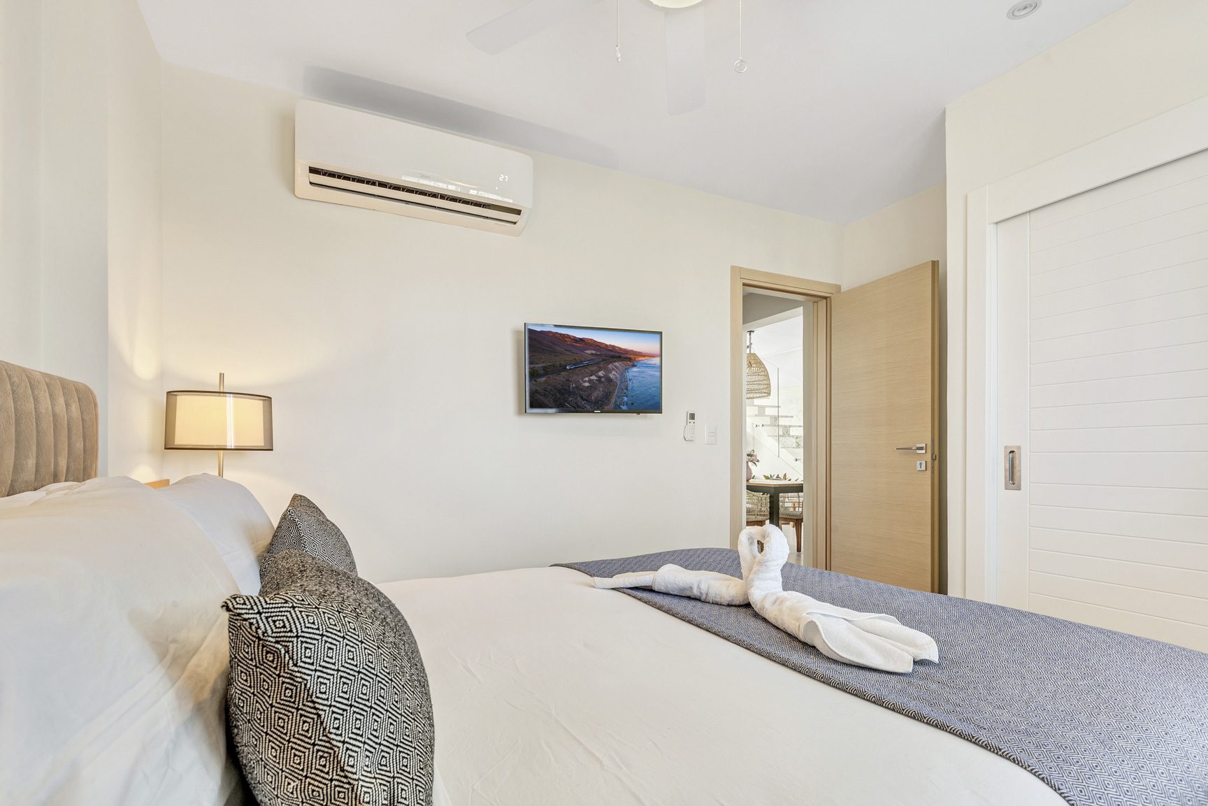 buyDRproperty Modern bedroom with swan towel art on bed, TV, and air conditioner. Clean, bright interior design. Sosua Real Estate