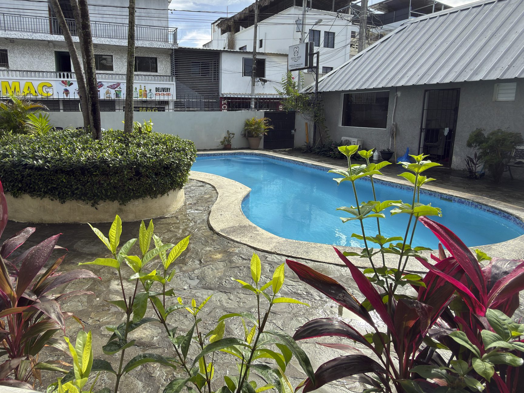 buyDRproperty Bright blue swimming pool surrounded by lush tropical plants and buildings. Sosua Real Estate