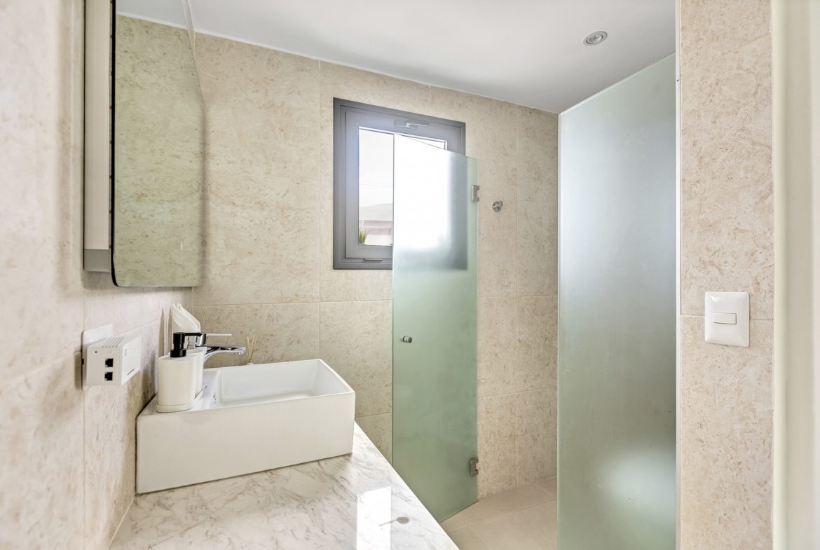 buyDRproperty Modern bathroom with square sink, marble countertop, frosted glass shower, and small window. Sosua Real Estate