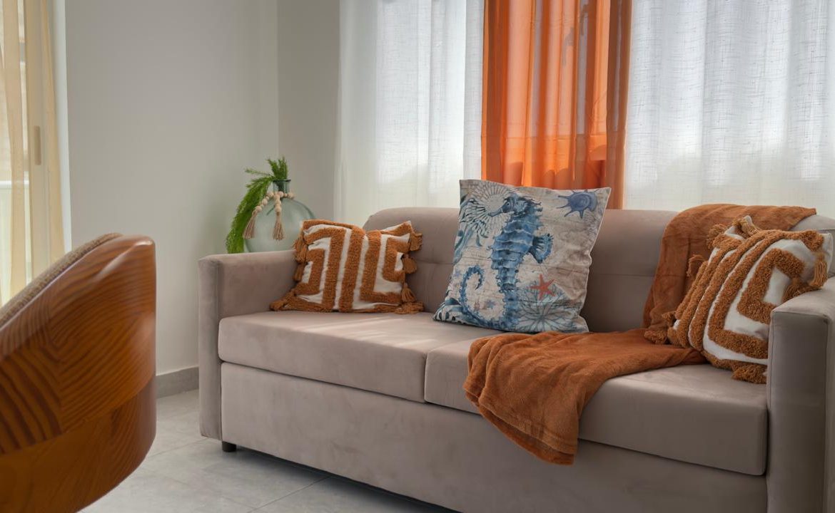 Beige sofa with decorative pillows and a throw blanket in a bright, airy living room.