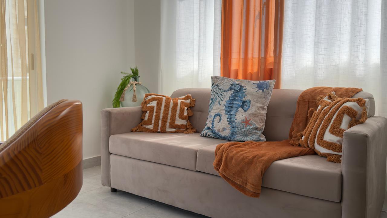 Beige sofa with decorative pillows and a throw blanket in a bright, airy living room.