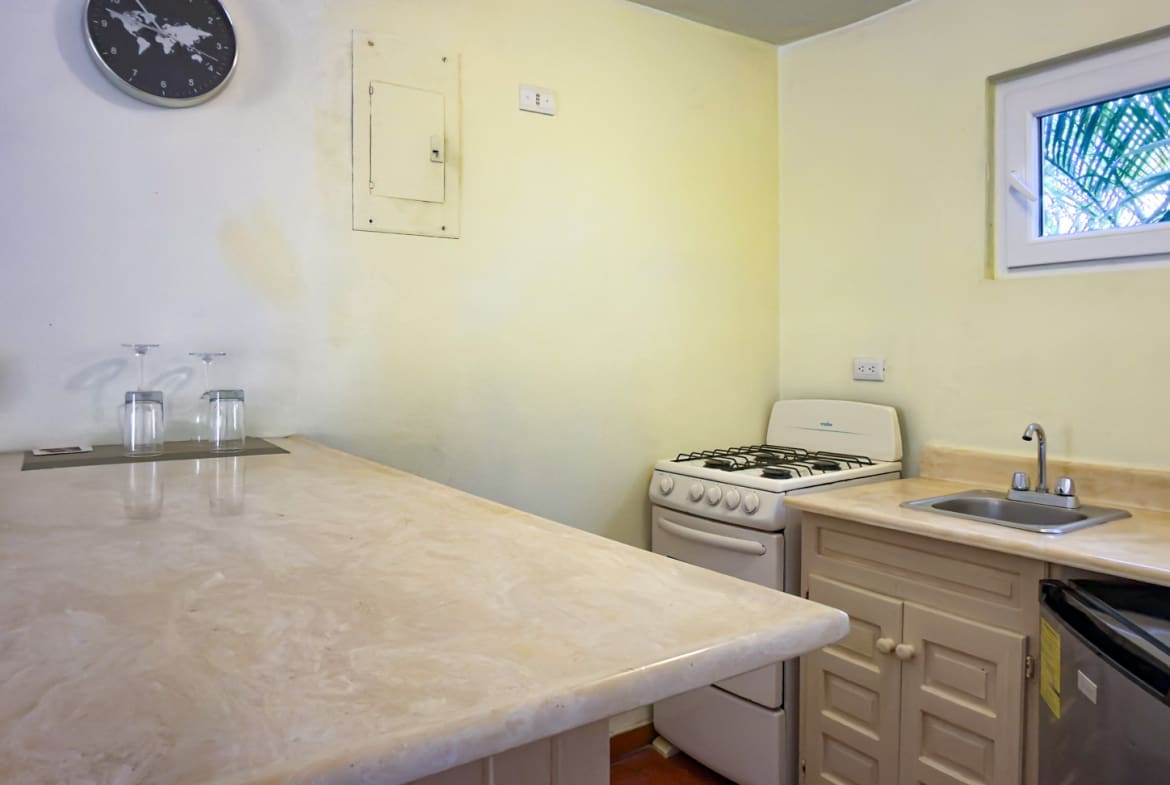 Compact kitchen with a marble countertop, stove, sink, and small refrigerator.