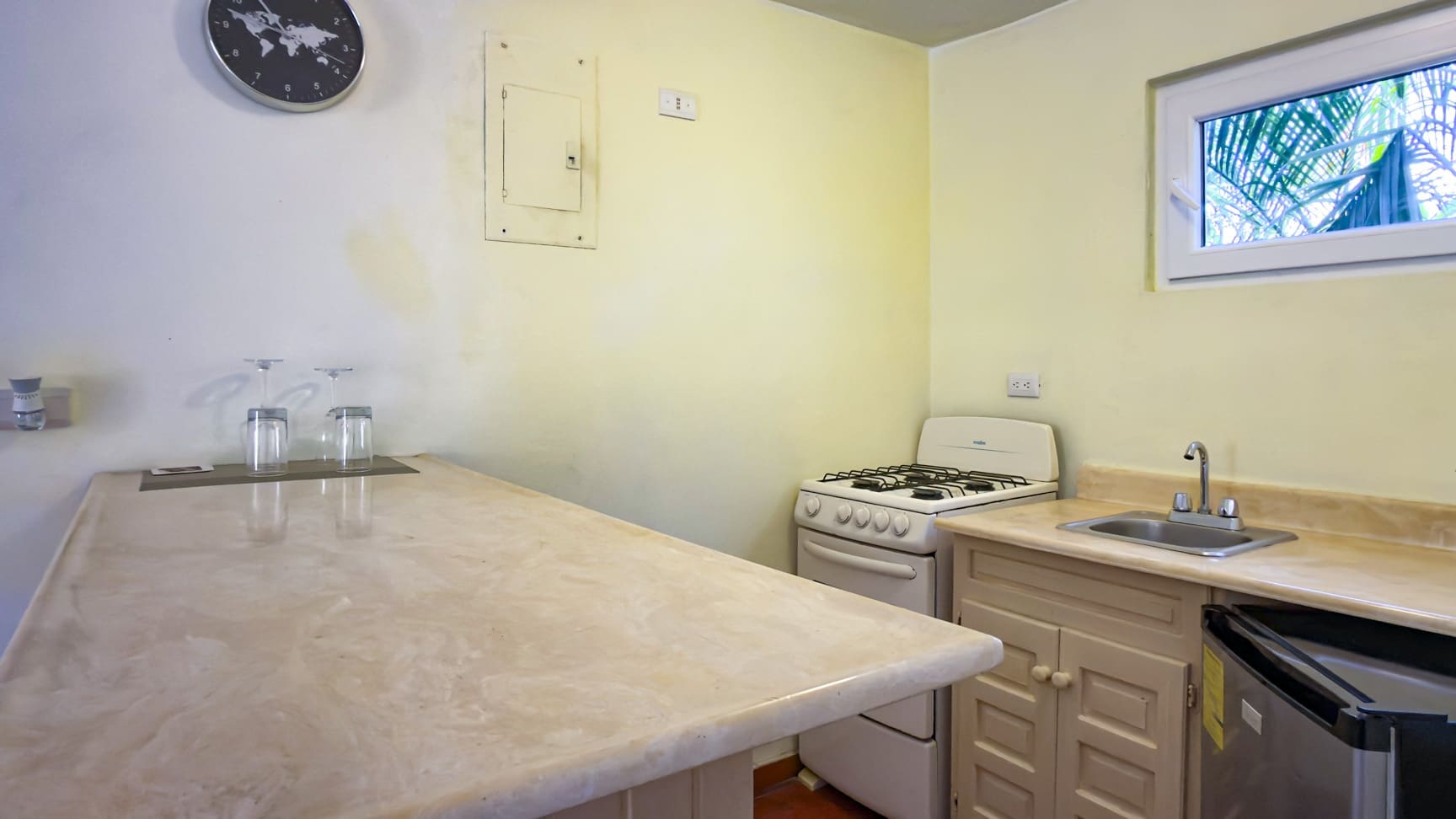 Compact kitchen with a marble countertop, stove, sink, and small refrigerator.