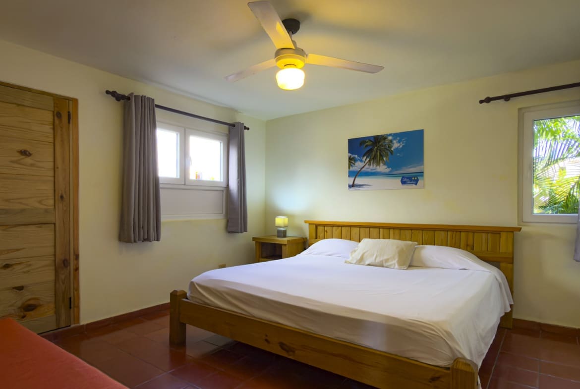 Spacious bedroom with bed, nightstands, ceiling fan, and tropical painting