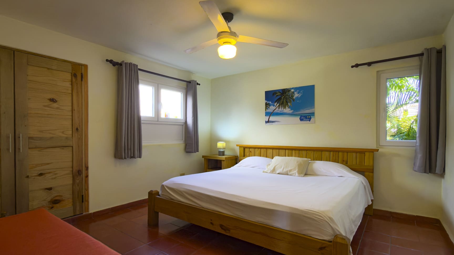 Spacious bedroom with bed, nightstands, ceiling fan, and tropical painting