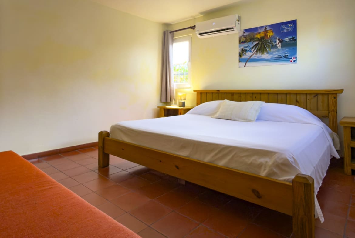 Wooden bed with white sheets in a cozy bedroom with red tiles