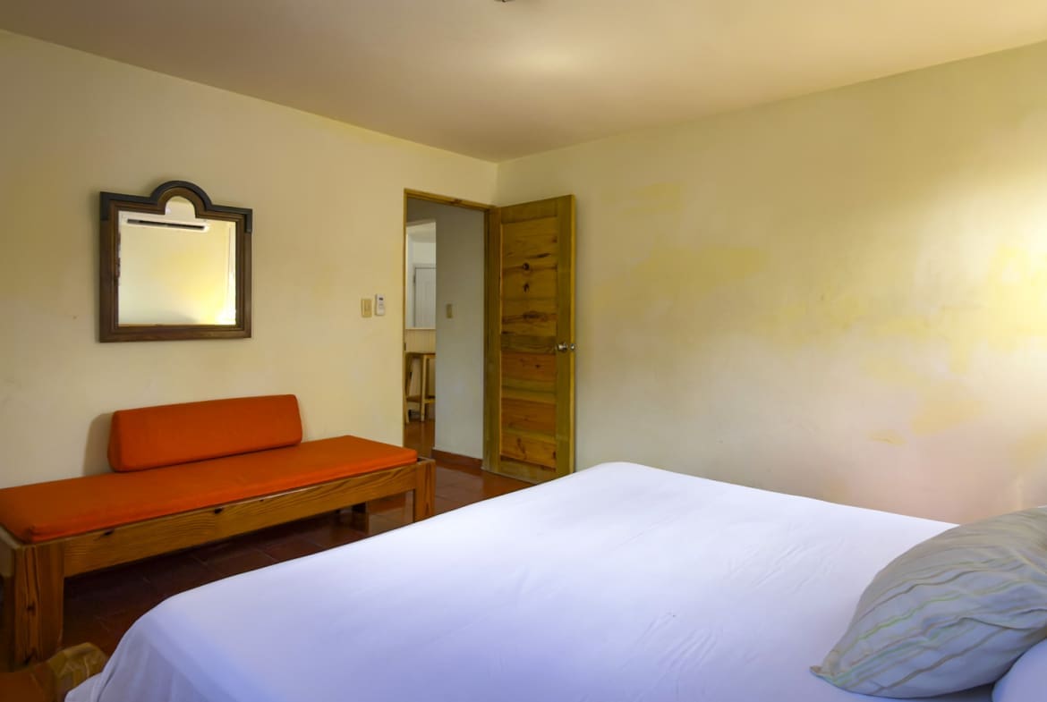 Bright hotel bedroom with white bedding, orange bench, and wooden mirror