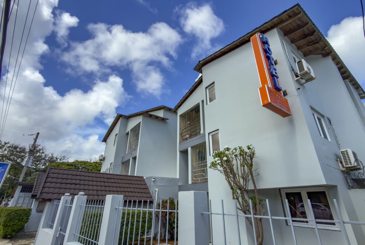 Hotel building with bright blue sky and clouds, featuring a neon sign.
