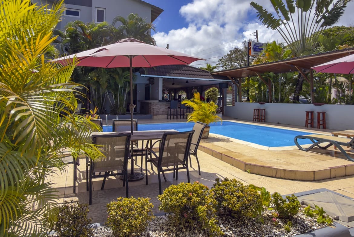 Resort pool with lounge chairs, umbrellas, and tropical plants in sunshine.