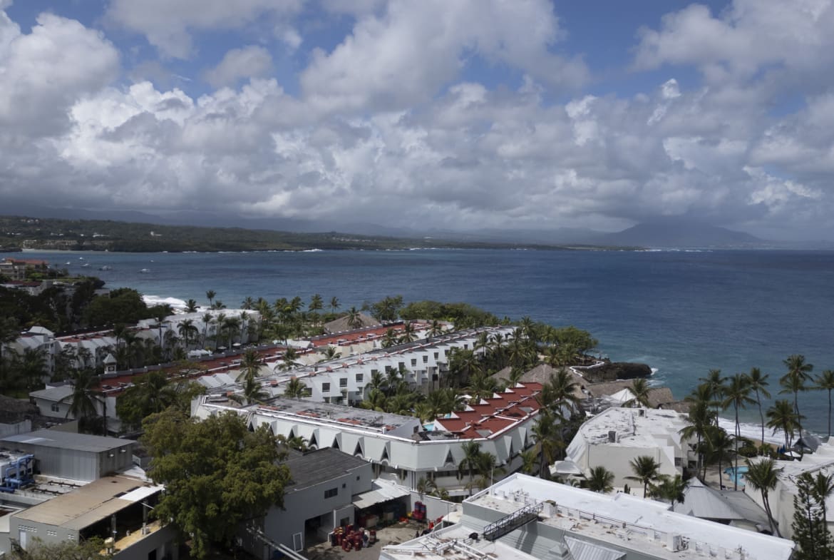 Aerial view of a coastal resort with white buildings and palm trees overlooking the ocean.