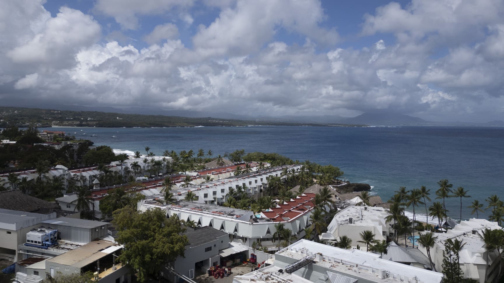 Aerial view of a coastal resort with white buildings and palm trees overlooking the ocean.