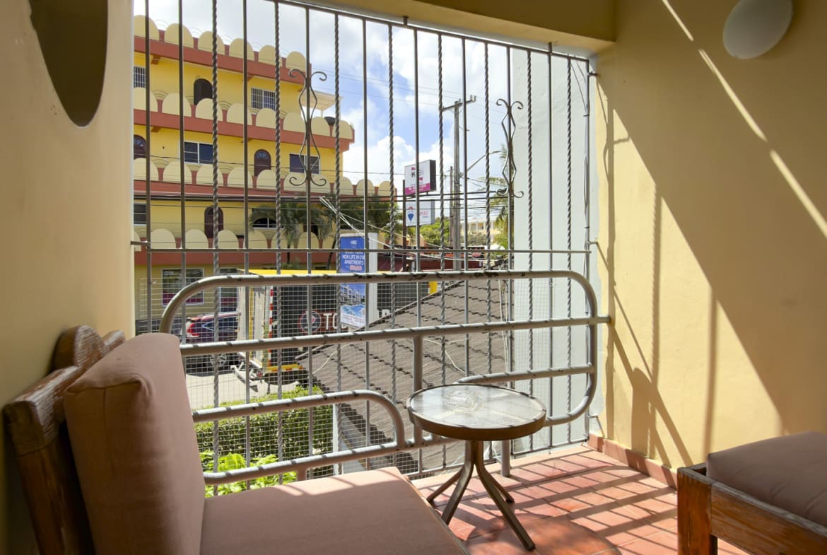 Balcony with chair and table overlooking a colorful building in a tropical city.