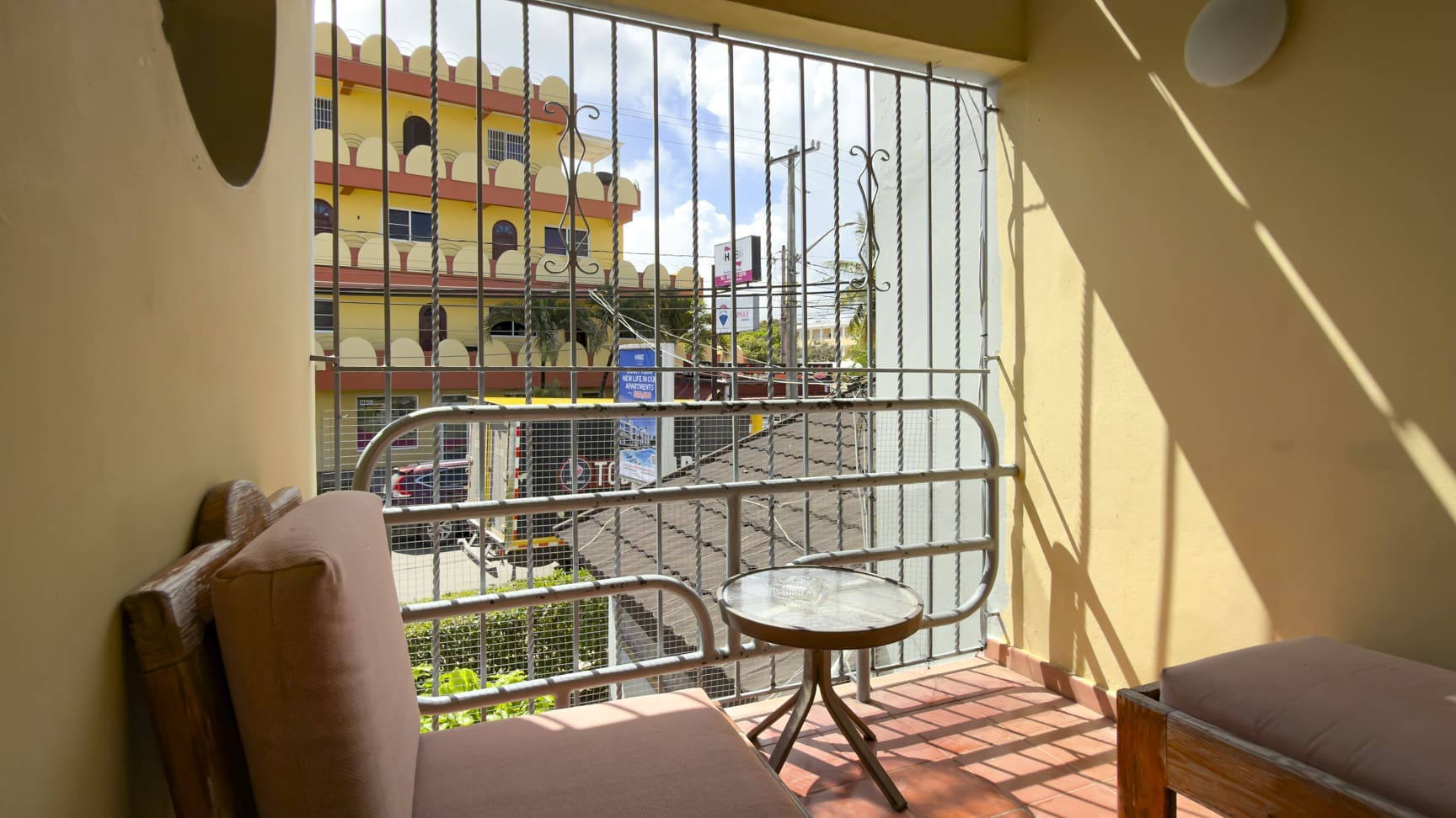 Balcony with chair and table overlooking a colorful building in a tropical city.