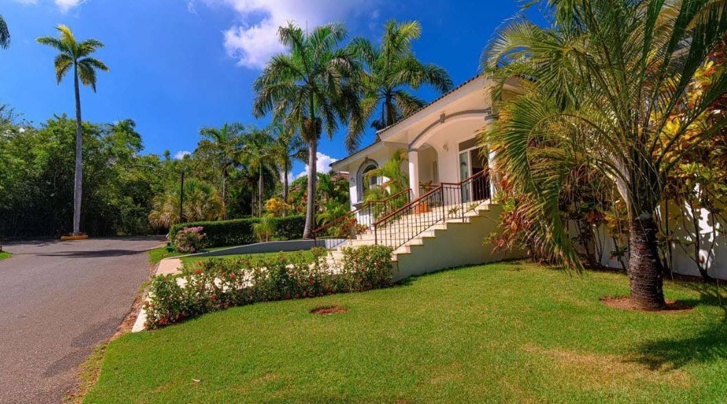 buyDRproperty Luxury villa with palm trees and lush green lawn in a tropical setting. Sosua Real Estate