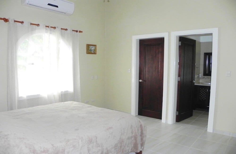 buyDRproperty Bedroom with a large bed, arched window with sheer curtains, and two doors leading to a bathroom. Sosua Real Estate