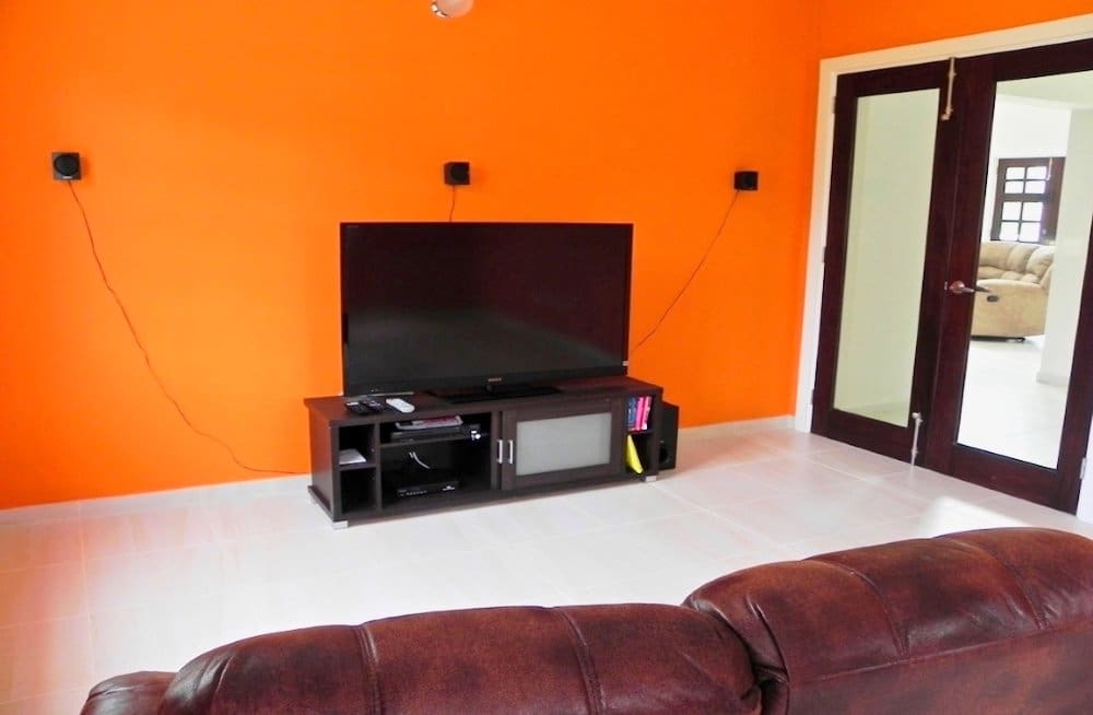 buyDRproperty Modern living room with large TV on stand, orange walls, and leather couch Sosua Real Estate