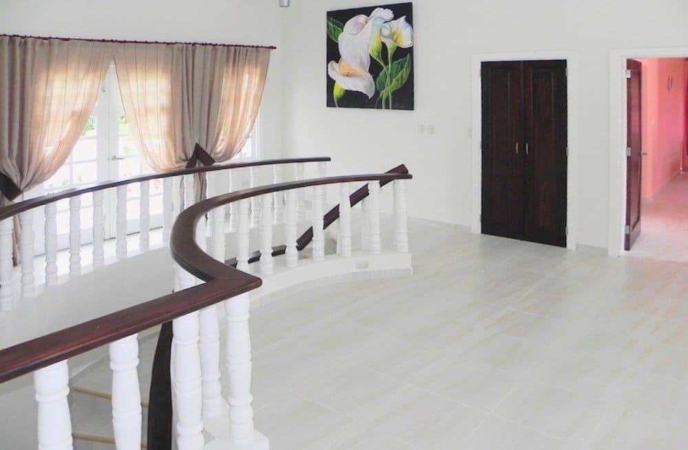 buyDRproperty Curved white staircase with dark wood railing in a bright, modern home hallway. Sosua Real Estate