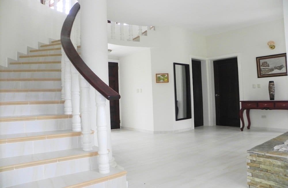 buyDRproperty Modern white foyer with a sweeping staircase and dark wood accents Sosua Real Estate
