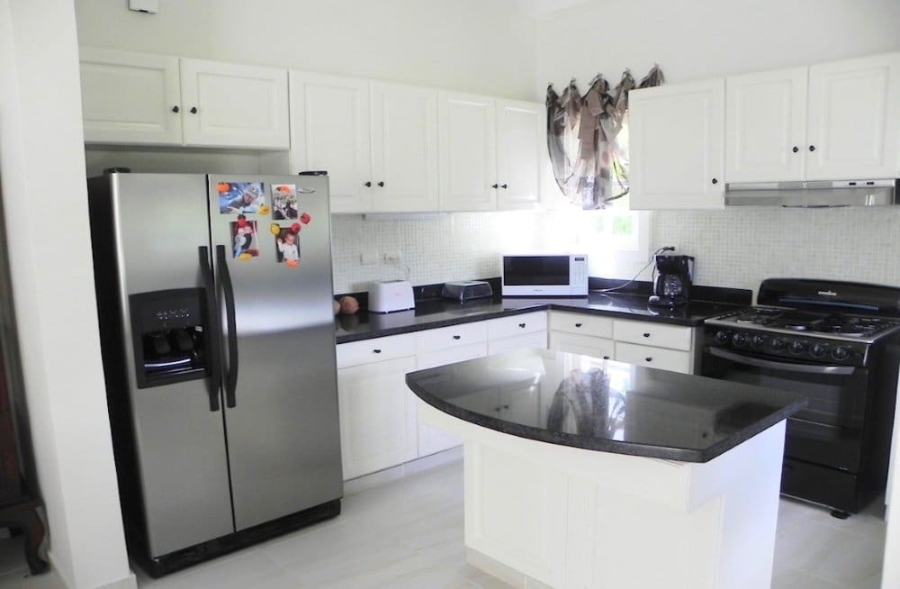 buyDRproperty Modern white kitchen with stainless steel refrigerator, granite island, and black stove. Sosua Real Estate