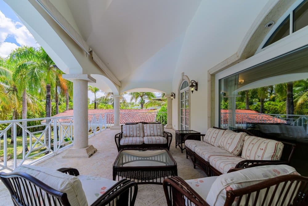 buyDRproperty Spacious covered balcony with wicker furniture, overlooking palm trees and a tiled roof. Sosua Real Estate