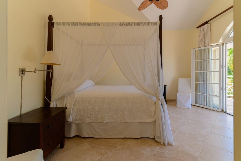buyDRproperty Four-poster bed with white drapes in a bright, airy bedroom with patio doors Sosua Real Estate