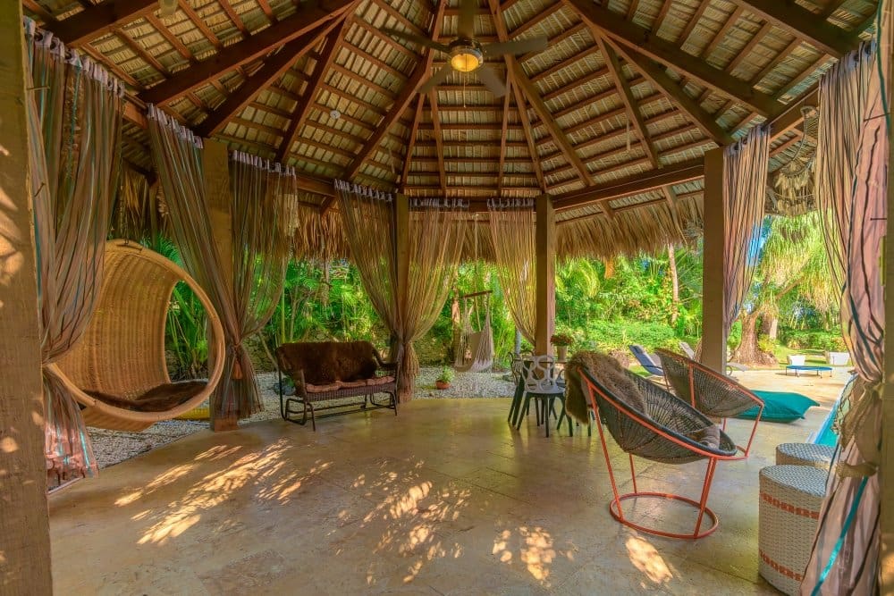 buyDRproperty Outdoor hexagonal patio with thatched roof, rattan chairs, and hanging chair. Sosua Real Estate