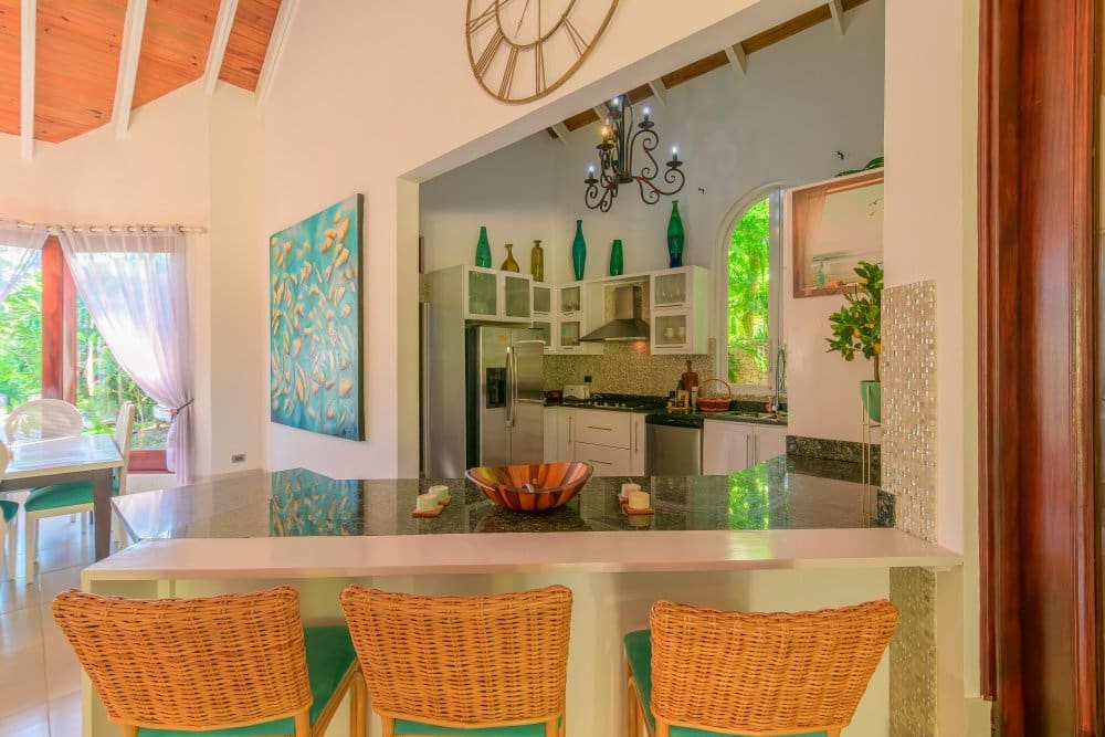 buyDRproperty Modern kitchen with granite island and wicker bar stools, featuring a chandelier and colorful decor. Sosua Real Estate