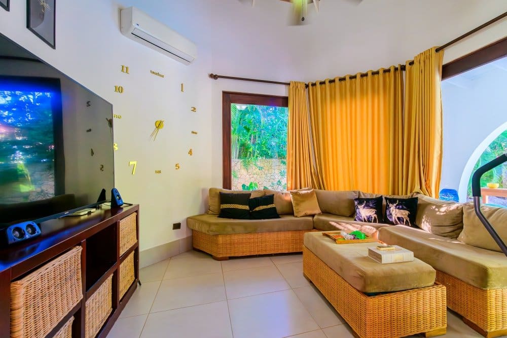 buyDRproperty Modern living room with a sectional sofa, large TV, and golden curtains. Sosua Real Estate