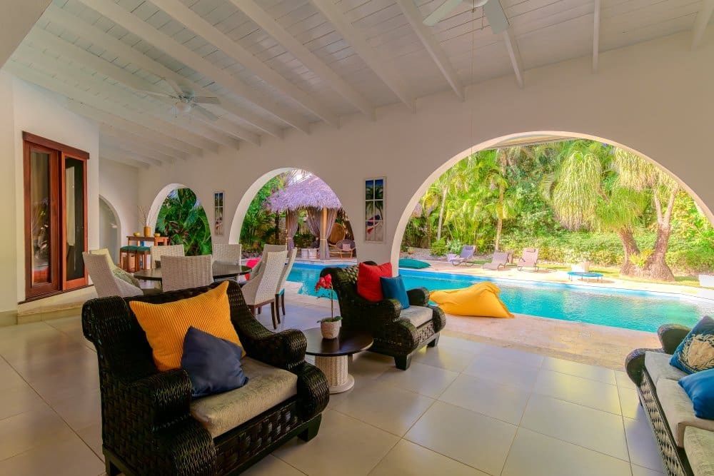 buyDRproperty Luxurious covered patio with comfortable seating overlooking a tropical pool and lush greenery. Sosua Real Estate