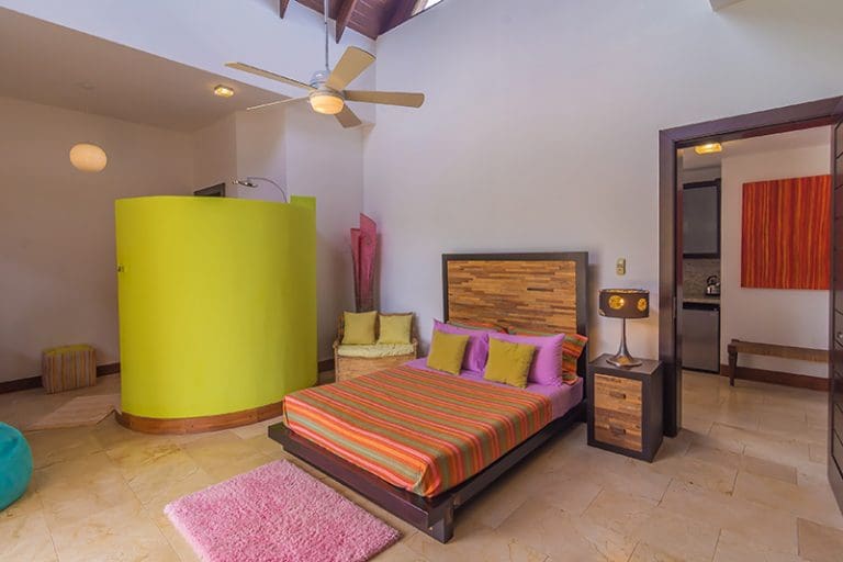 buyDRproperty Modern bedroom with bright green shower enclosure and colorful striped bedding. Sosua Real Estate
