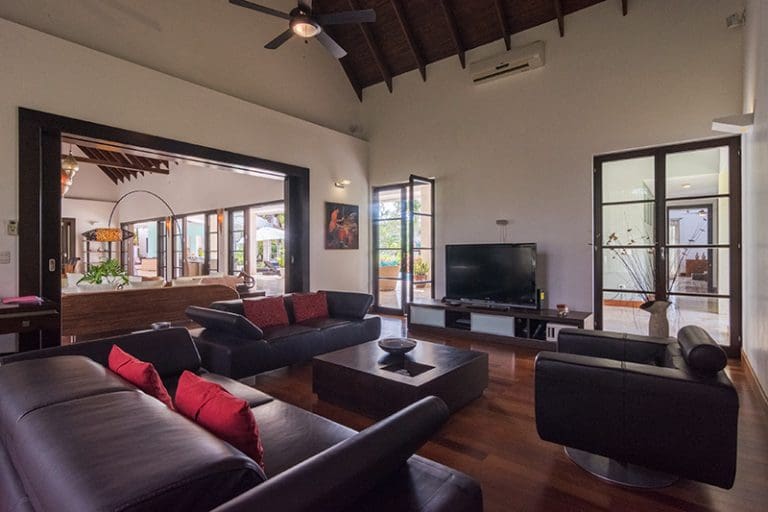 buyDRproperty Spacious modern living room with dark leather sofas, large TV, and sliding glass doors opening to a patio. Sosua Real Estate