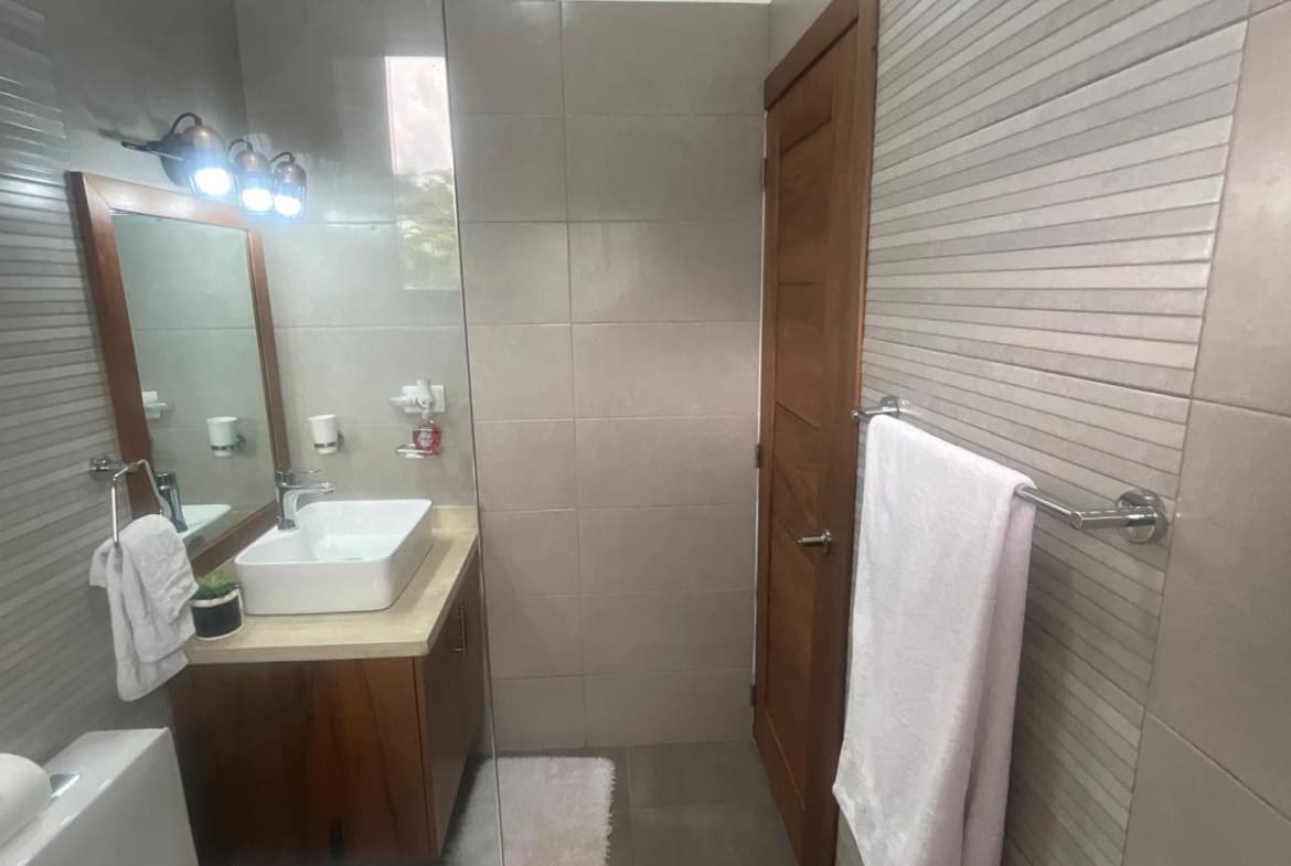 buyDRproperty Modern bathroom with a square sink, wooden vanity, and glass shower enclosure. Sosua Real Estate