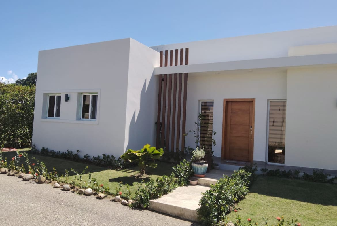 buyDRproperty Modern white house exterior with wooden accents and lush landscaping. Sosua Real Estate