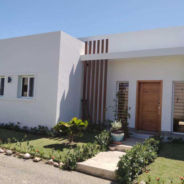 buyDRproperty Modern white house exterior with wooden accents and lush landscaping. Sosua Real Estate